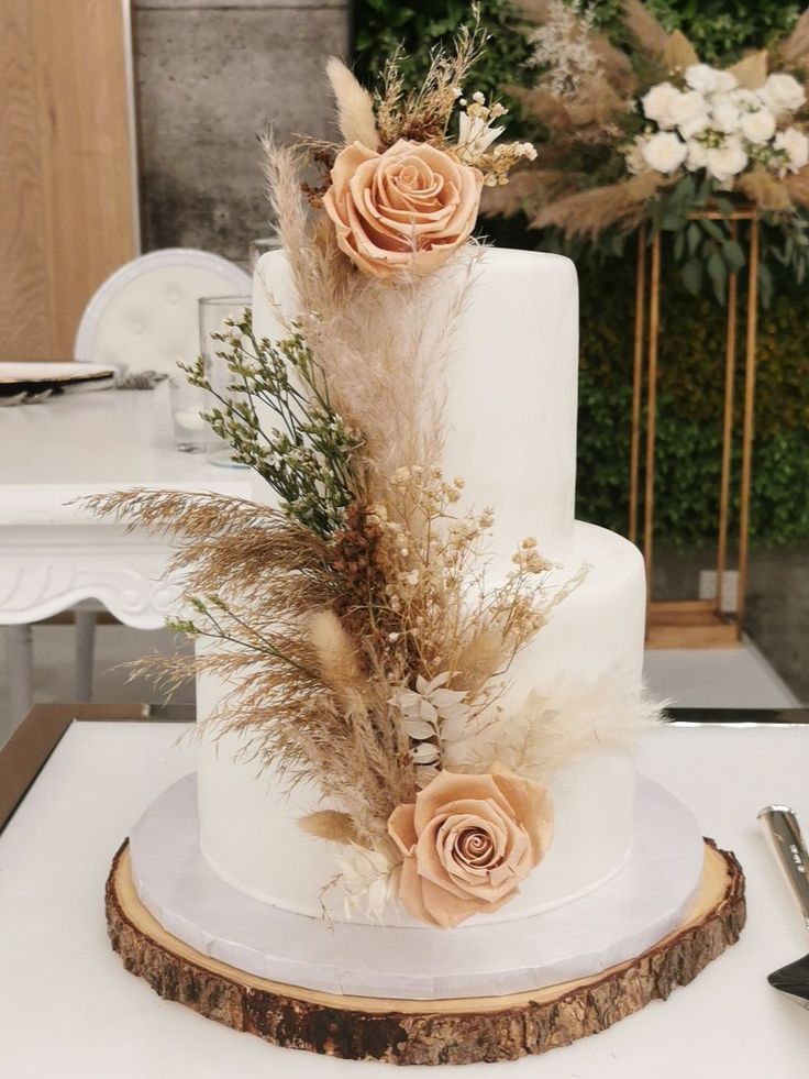 a three tiered cake with flowers and feathers on the top is sitting on a table