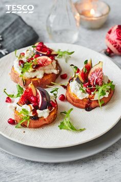 a white plate topped with crostini covered in cheese and toppings next to a candle