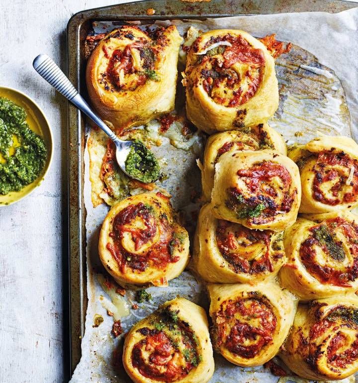 a tray filled with different types of pastries next to a bowl of pesto sauce