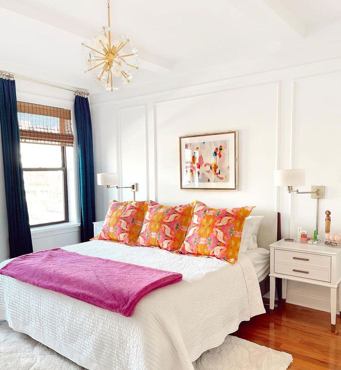 a white bed topped with lots of pillows next to a window