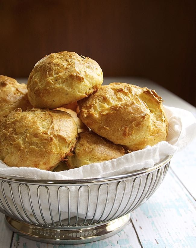 a bowl full of biscuits sitting on top of a wooden table with the words gruyere gougeres