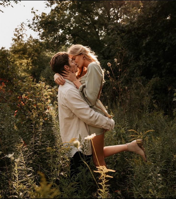 a man and woman kissing in the middle of tall grass with trees in the background