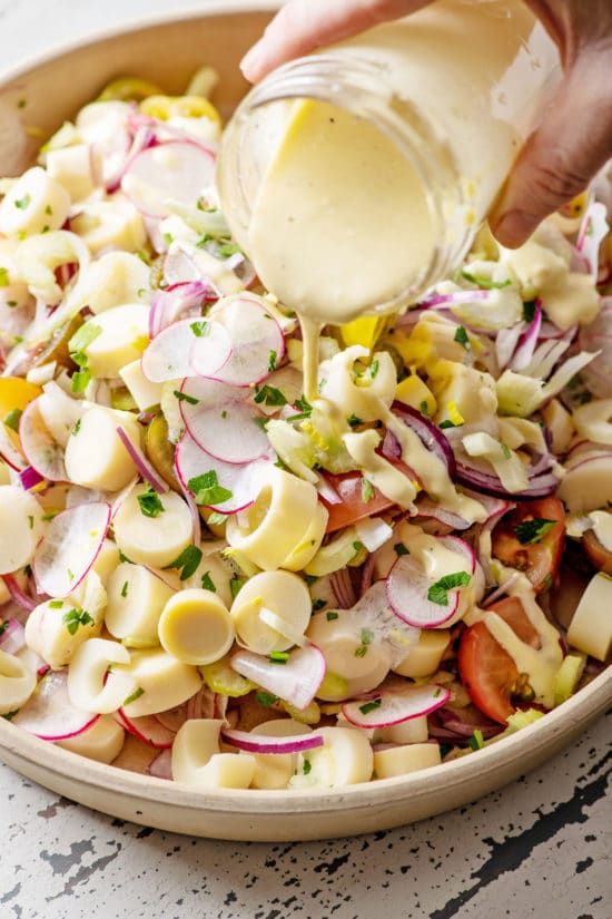 a person pouring dressing into a bowl filled with pasta salad