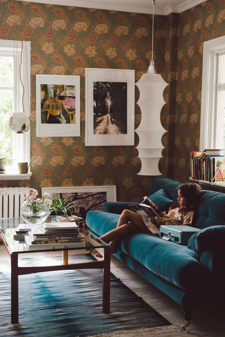 a woman sitting on top of a blue couch in a living room next to a window