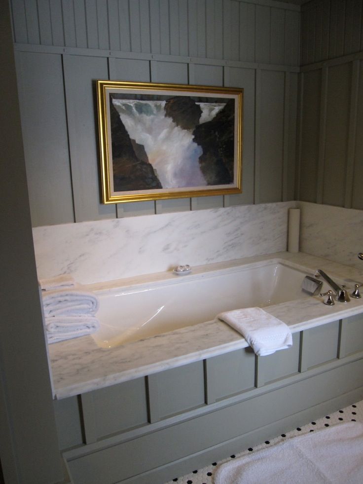 a white bath tub sitting in a bathroom next to a painting on the wall above it