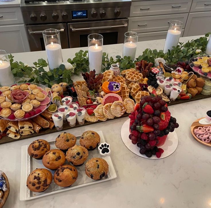 a table filled with lots of food on top of a white counter next to candles