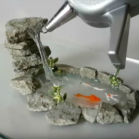 a person is pouring water into a small pond with rocks and plants on the side