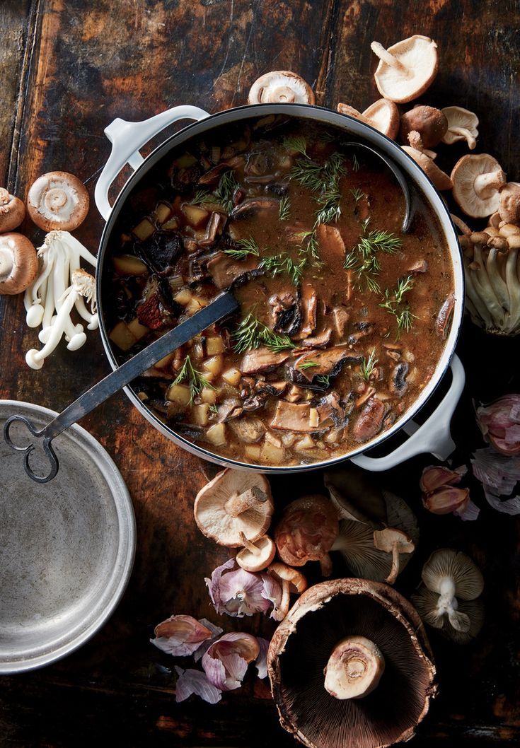 a pot full of mushroom soup next to mushrooms and other vegetables on a wooden table