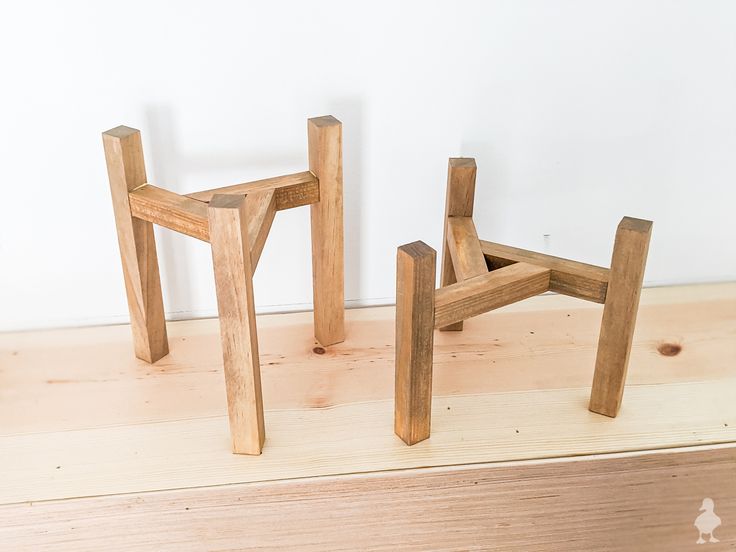 two wooden stools sitting next to each other on top of a wood floor in front of a white wall