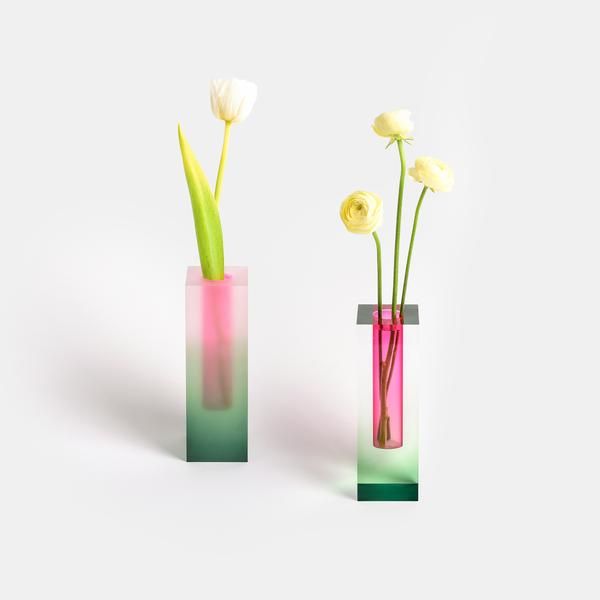 two vases with flowers in them sitting side by side on a white surface, one is pink and the other is green