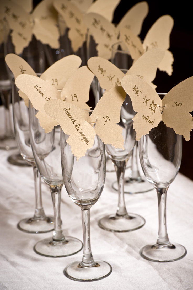 many wine glasses are lined up on a table with place cards in the shape of butterflies