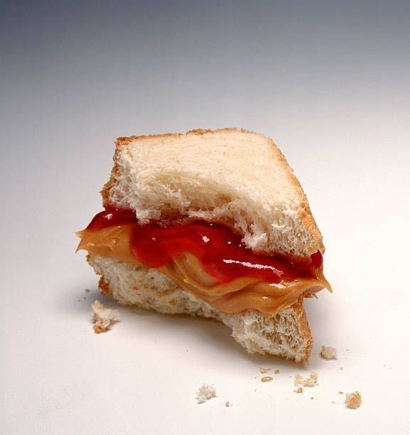 a half eaten sandwich with ketchup on it sitting on top of a white surface