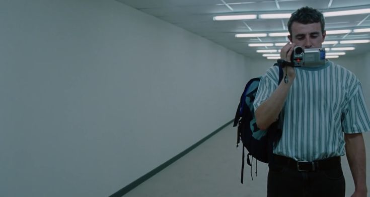 a man walking down a hallway while holding a camera to his face and talking on the phone