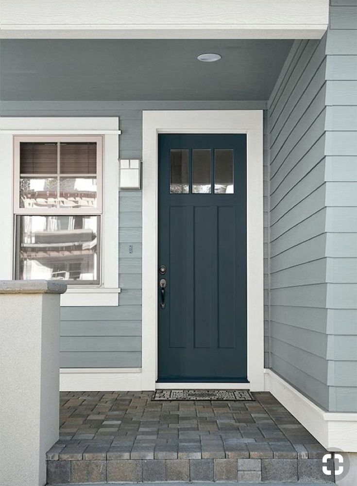 a blue front door on a gray house with white trim and brick steps leading up to it