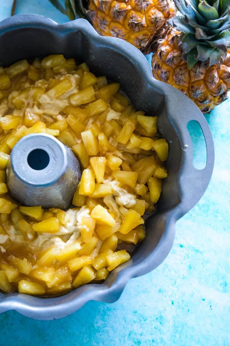 a pineapple upside down cake in a metal pan next to two pineapples