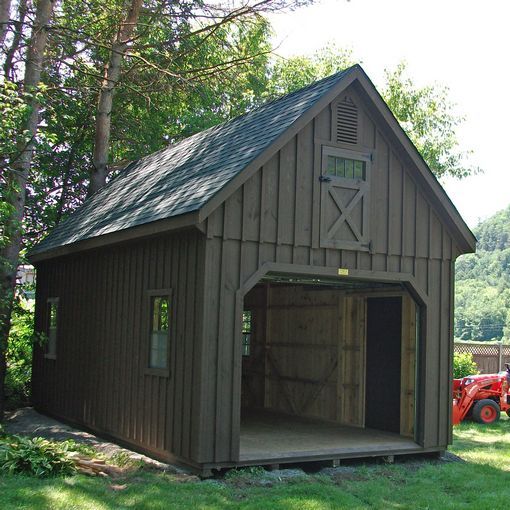 a barn with a red tractor parked in the yard next to it and trees around