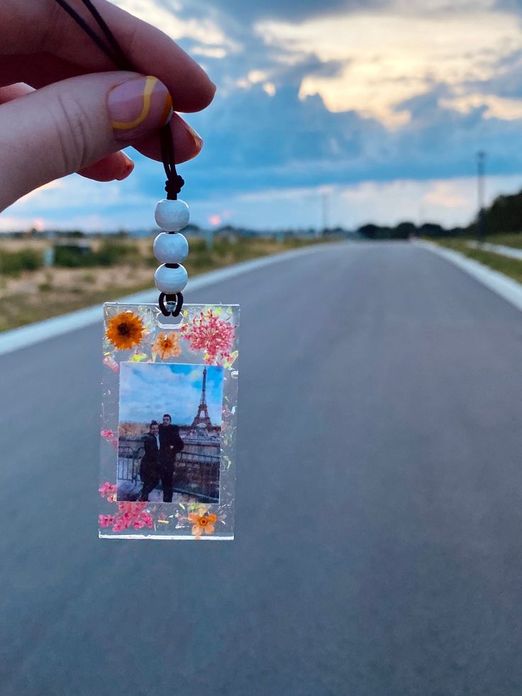 a person holding up a photo on the side of a road with flowers in it