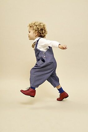 a young child is running while wearing overalls and red shoes with one foot in the air