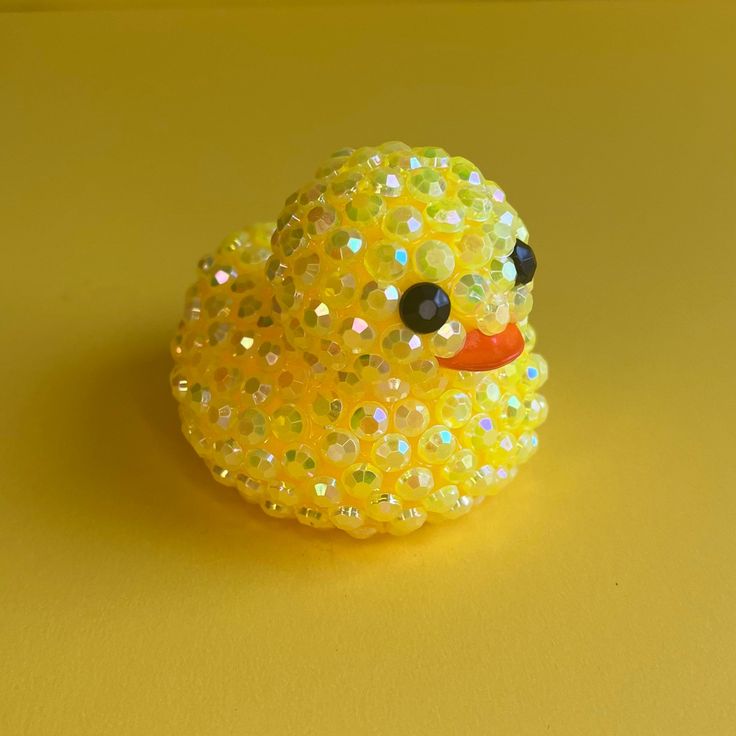 a yellow rubber duck with sequins on it's head sitting on a yellow surface