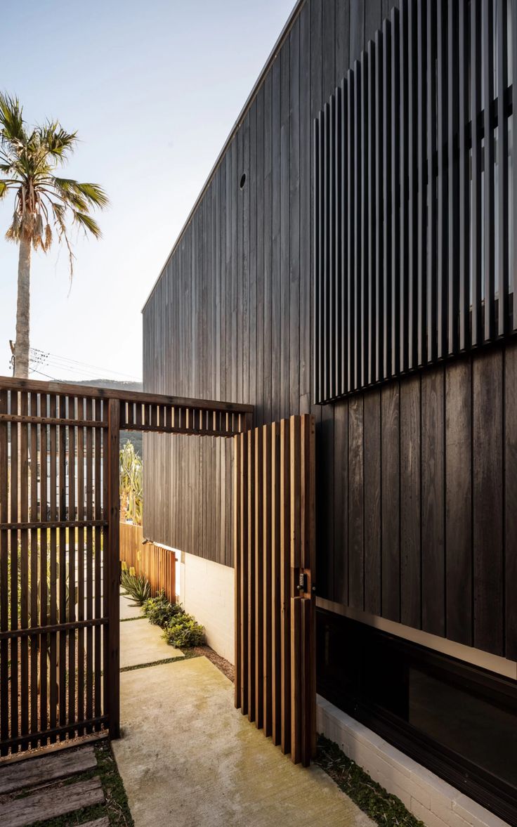 an entrance to a building with wooden slats on the side and palm trees in the background