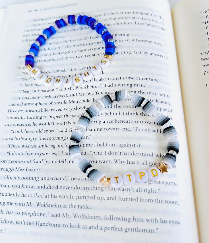 a blue and white beaded bracelet sitting on top of an open book with words written in gold