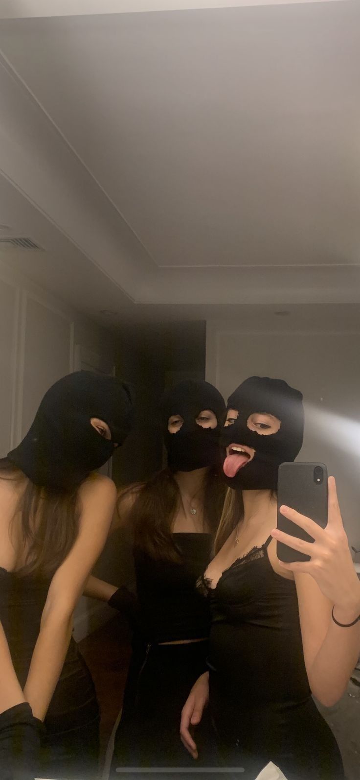 three women in black dresses and masks taking a selfie