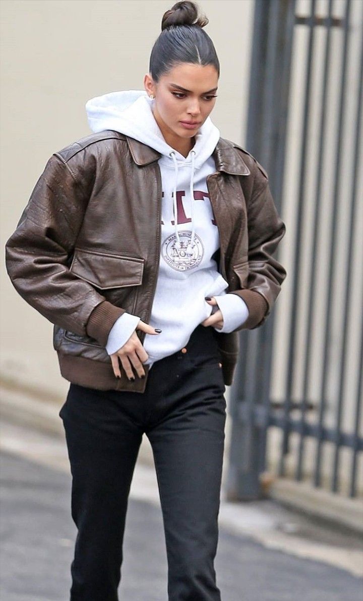 a woman walking down the street wearing black pants and a brown leather jacket with hoodie