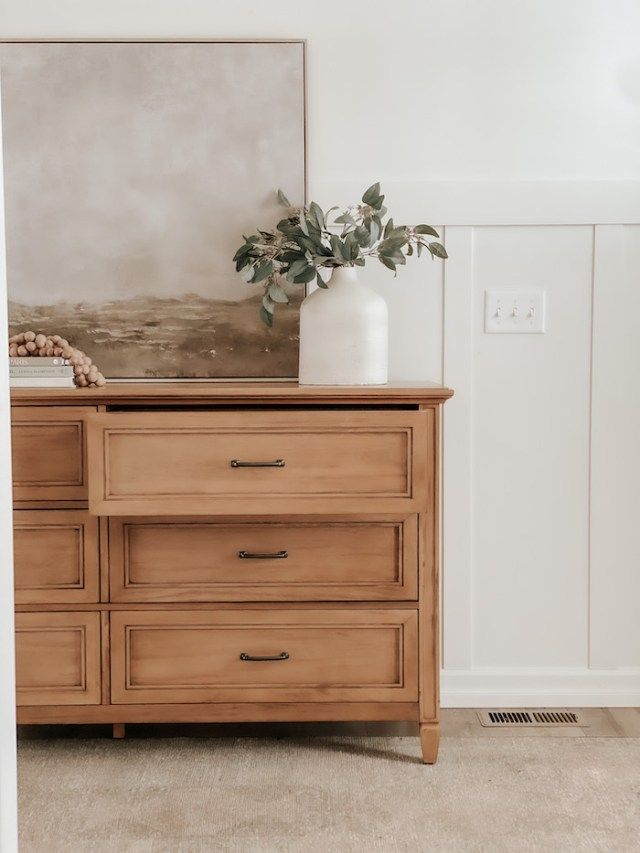 a wooden dresser with two vases and a painting on the wall in the background