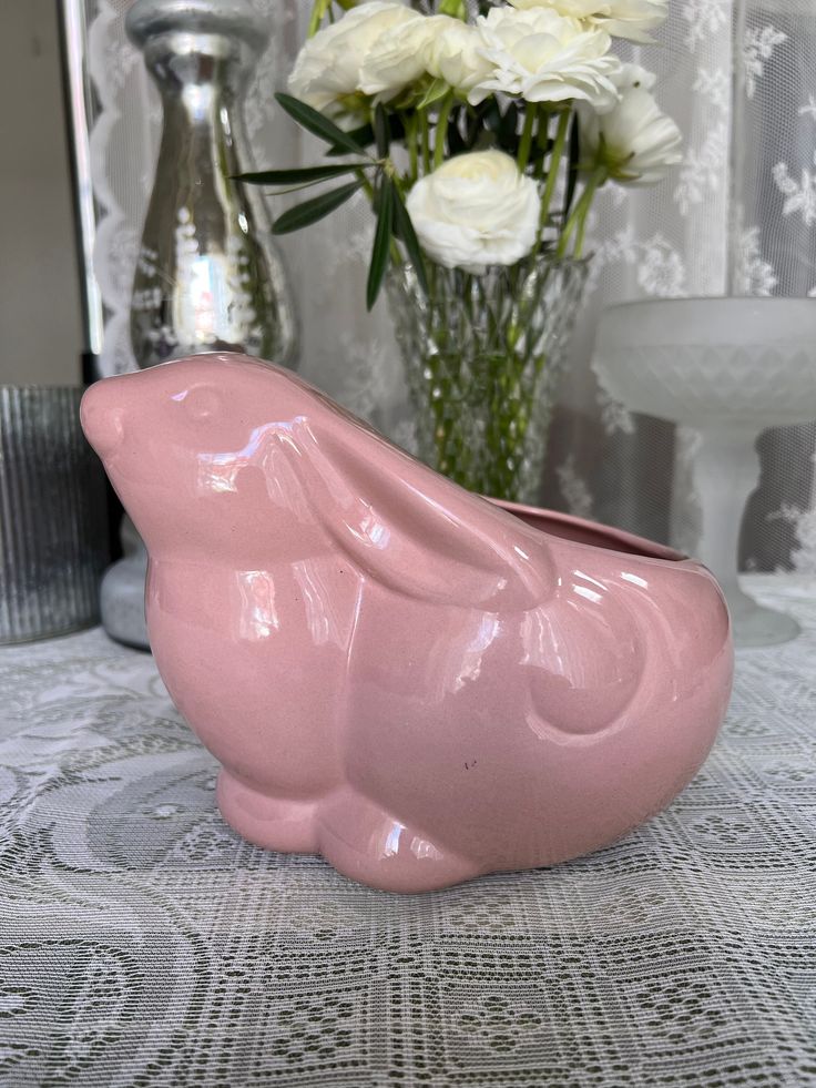 a pink bird shaped vase sitting on top of a table next to a vase filled with white flowers