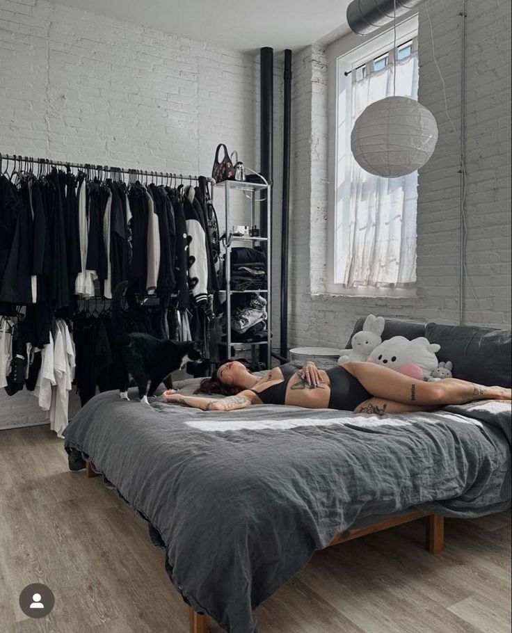 a woman laying on top of a bed in a room with lots of clothes hanging