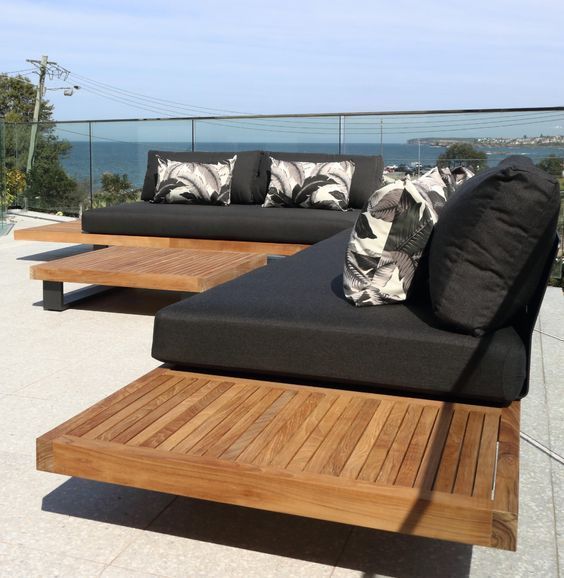 a wooden couch sitting on top of a patio next to a large body of water