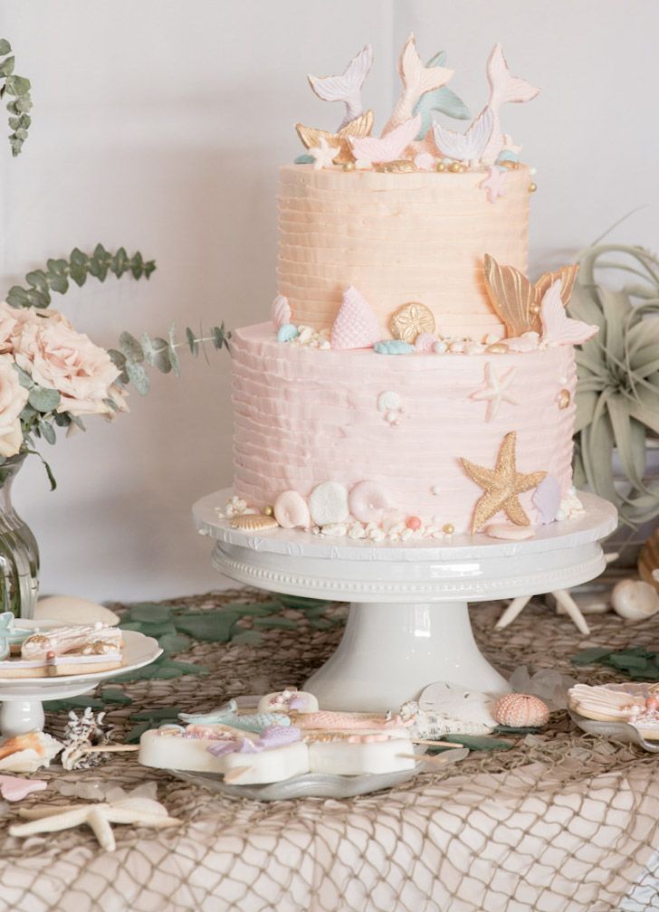 there is a pink cake on the table with shells and other items around it,