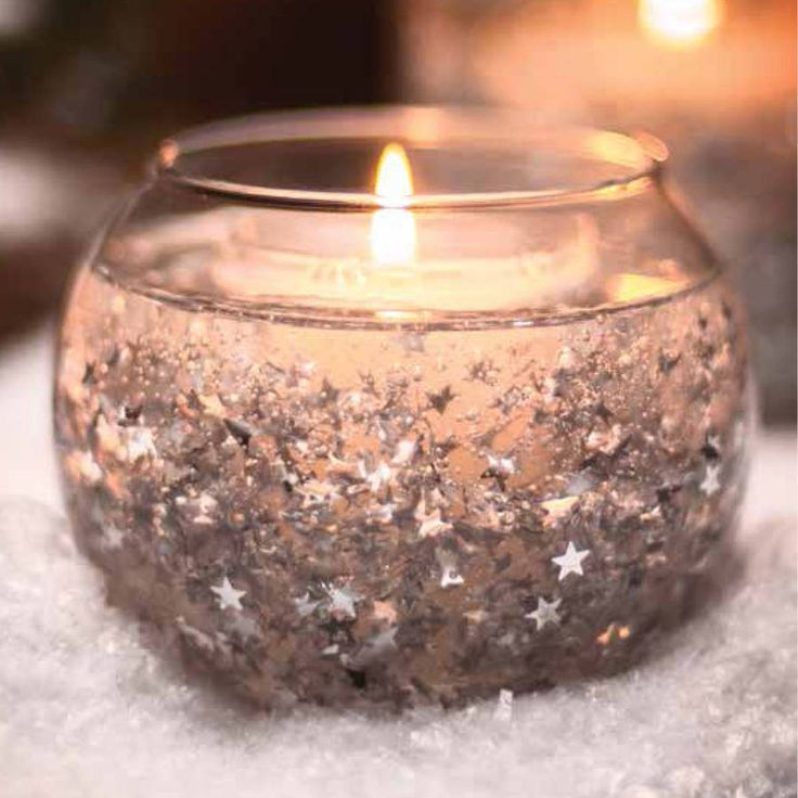 a candle that is sitting in the snow with stars on it's glass bowl