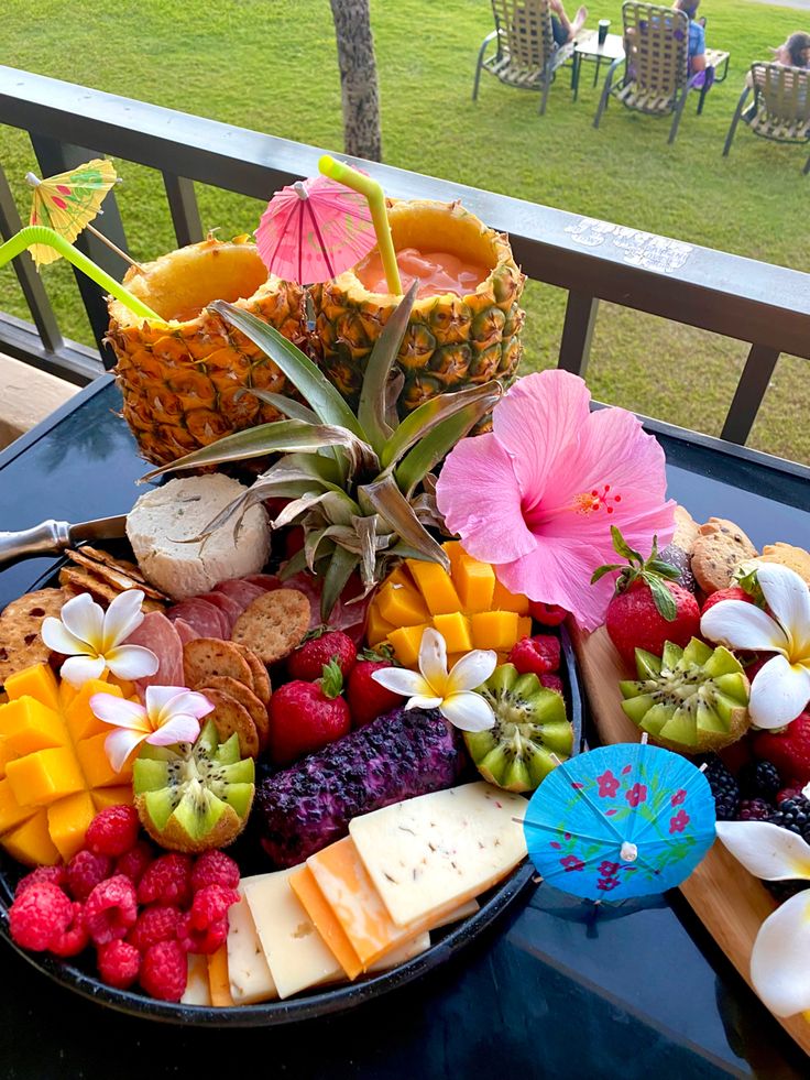 a platter filled with fruit and cheese on top of a table next to an umbrella