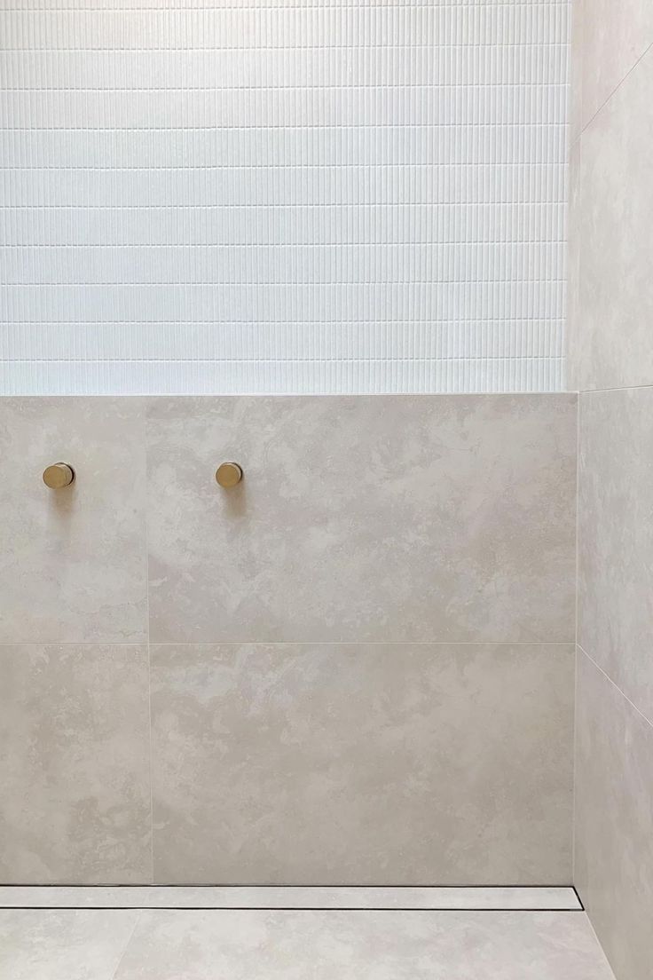 a white tiled bathroom with two brass fixtures on the wall and tile flooring in the shower