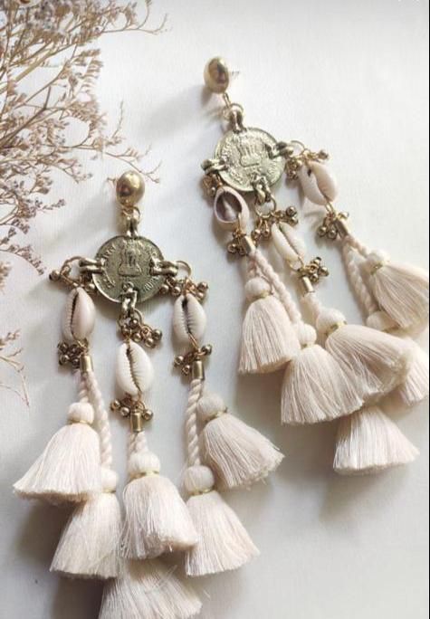 TICKLED BY TASSELS WHAT IT IS: Cowrie tasseled drop earrings WHY IT’S SPECIAL: Dramatically different with it's combination of materials, textures and extra-long length Statement earrings with a chic bohemian vibe GOOD TO KNOW: Cotton Fringe, brass, coins and cowrie shells Weight 25 grams Length 16.5 cm Available in blush and Snow White WHY WE LOVE RITIKA SACHDEVA: Handmade in India, Ritika Sachdeva puts a quirky take on traditional designs. Her jewelry turns heads with their oversized and uniqu Handmade Traditional Jewelry, Luxury Chandelier Earrings With Latkans For Reception, Cheap Silver Jewelry With Latkans, Luxury Silver Jewelry With Latkans, White Bohemian Jewelry With Dangling Charms, Cheap Chandelier Earrings With Latkans For Parties, Luxury Festive Jewelry With Latkans, Beaded Cowrie Shell Jewelry, White Latkans Earrings For Navratri