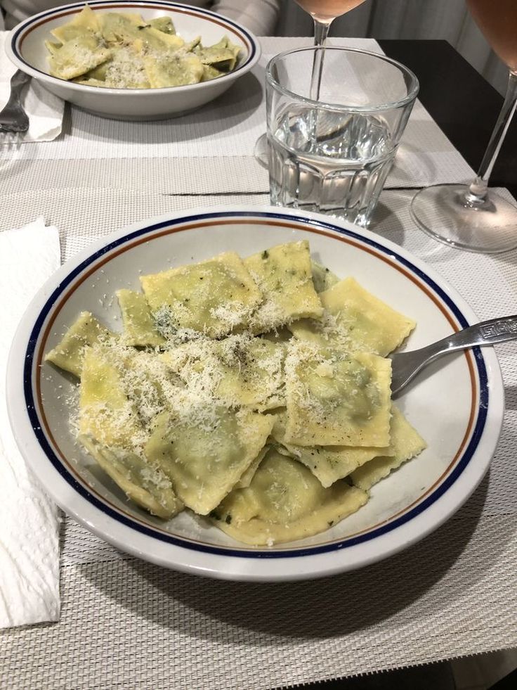 a white plate topped with ravioli next to a glass of wine on a table