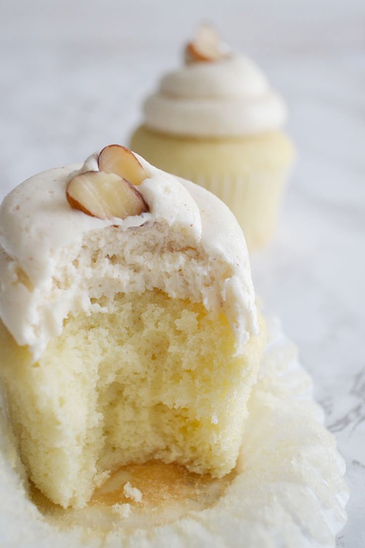 two cupcakes with white frosting and nuts on top, one half eaten