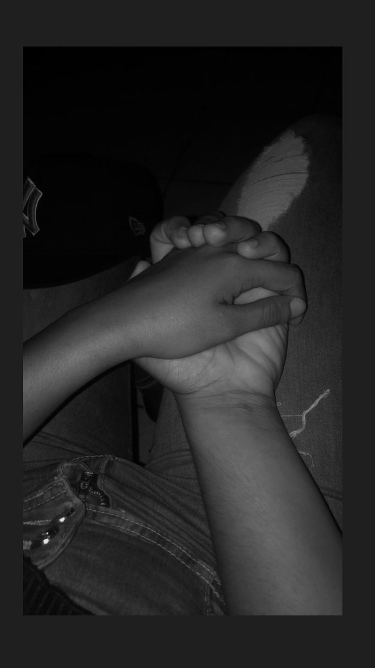 black and white photo of two people's hands holding each other while sitting on a couch