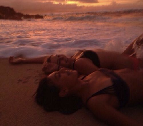 two people laying on the beach at sunset