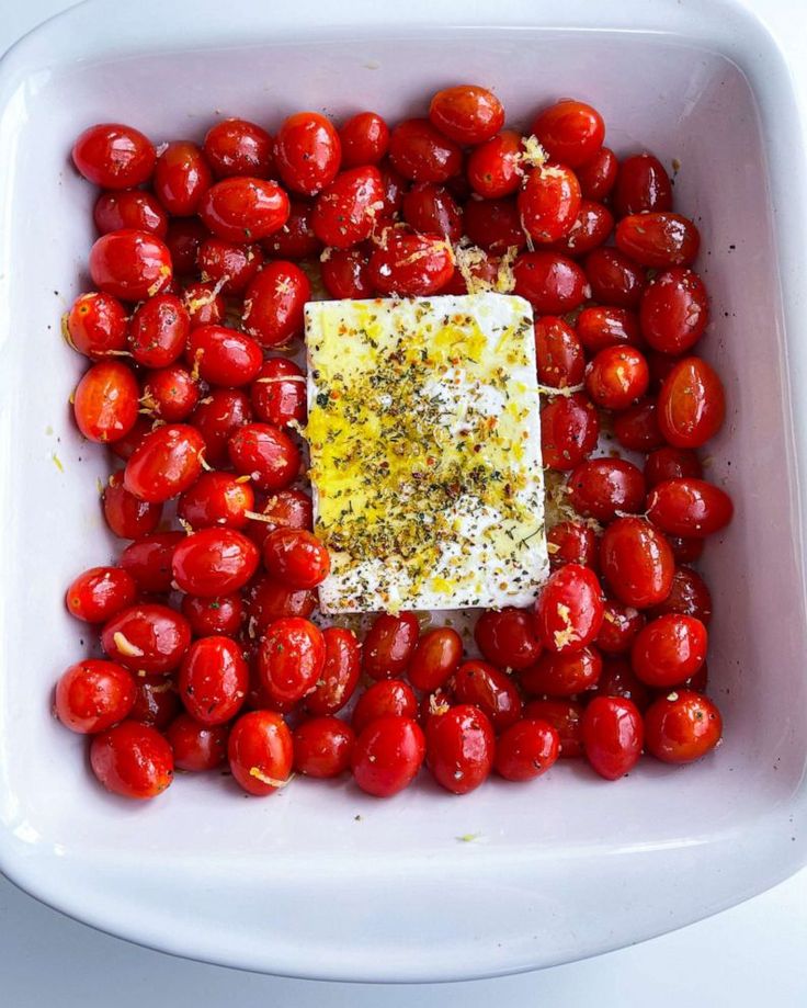 a square white bowl filled with tomatoes and seasoning