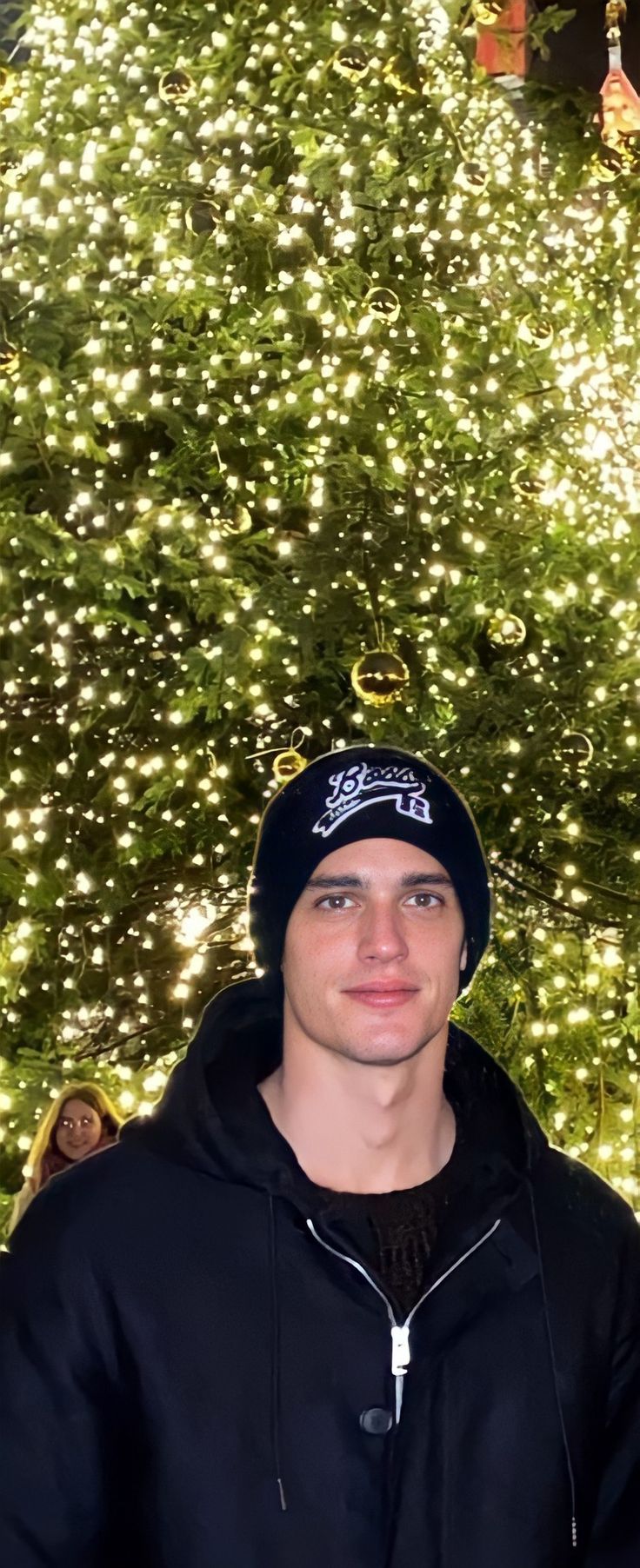 a man standing in front of a large christmas tree with lights on it's sides