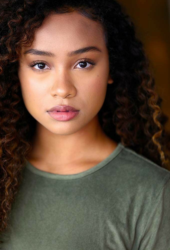 a close up of a person wearing a green shirt with curly hair and blue eyes