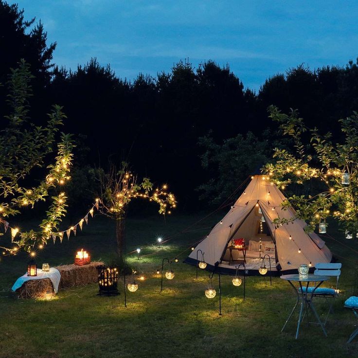 a tent is lit up at night with candles in the grass and trees around it