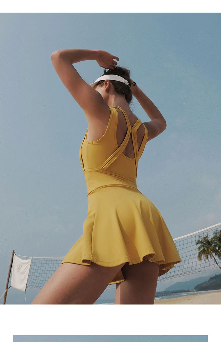 a woman in a yellow dress on the beach with a tennis racket and ball