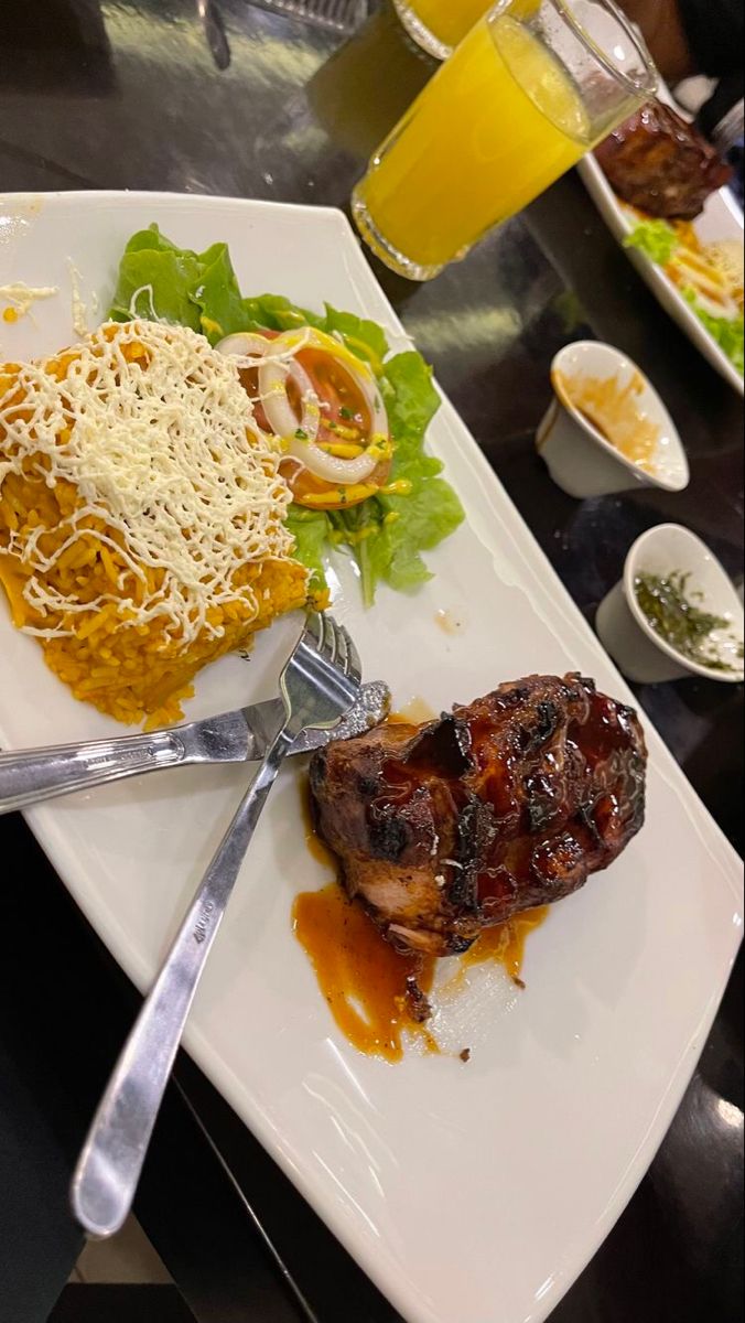 a plate with meat, rice and salad on it next to a glass of orange juice