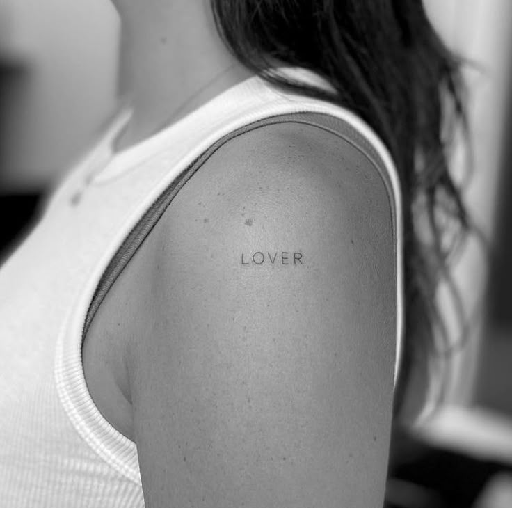 a woman with a tattoo on her shoulder that says lover in cursive writing