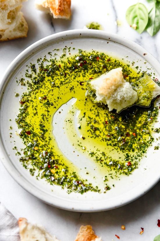 a white bowl filled with pesto and bread on top of a marble countertop