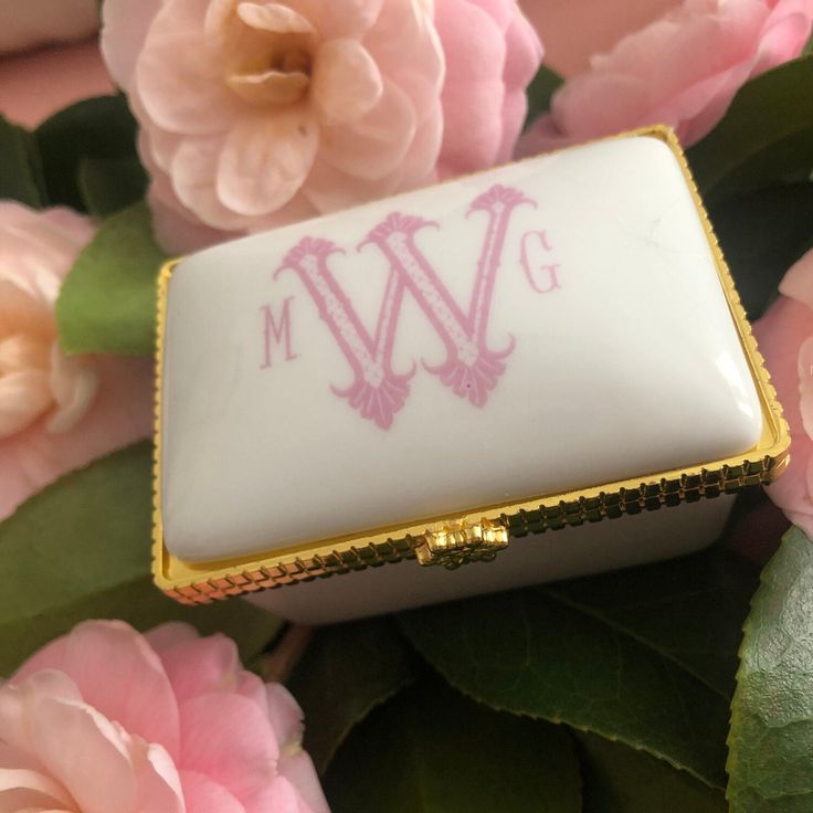 a white and gold purse with the letter w on it sitting next to pink flowers