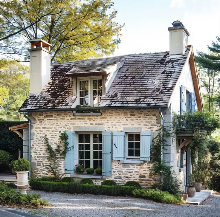 a stone house with blue shutters on the front and side windows, surrounded by greenery